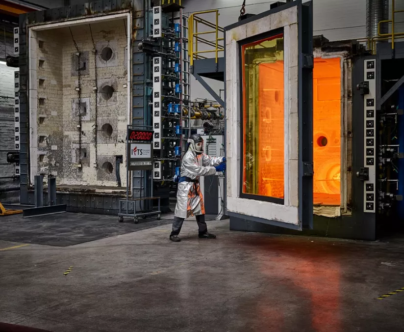 Fire resistance testing in a laboratory with a person in a protective suit standing between two large furnaces