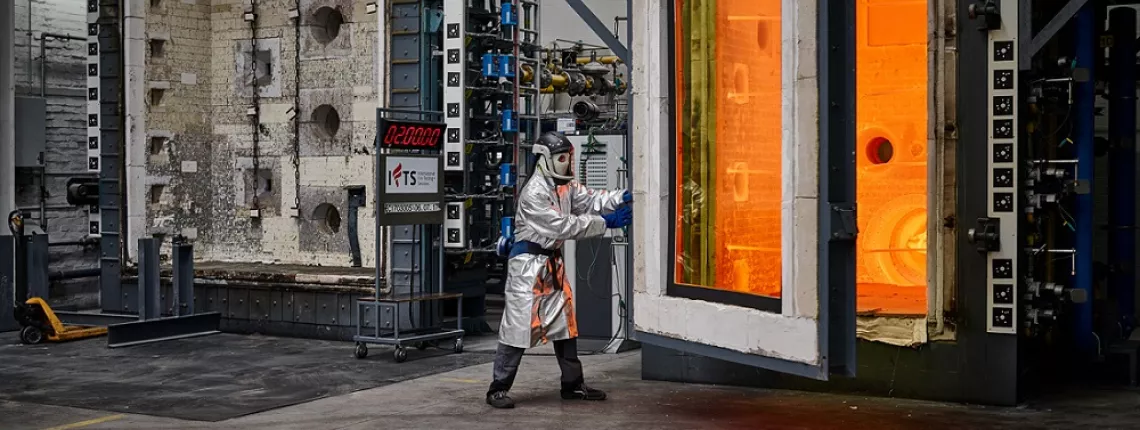 Fire resistance testing in a laboratory with a person in a protective suit standing between two large furnaces
