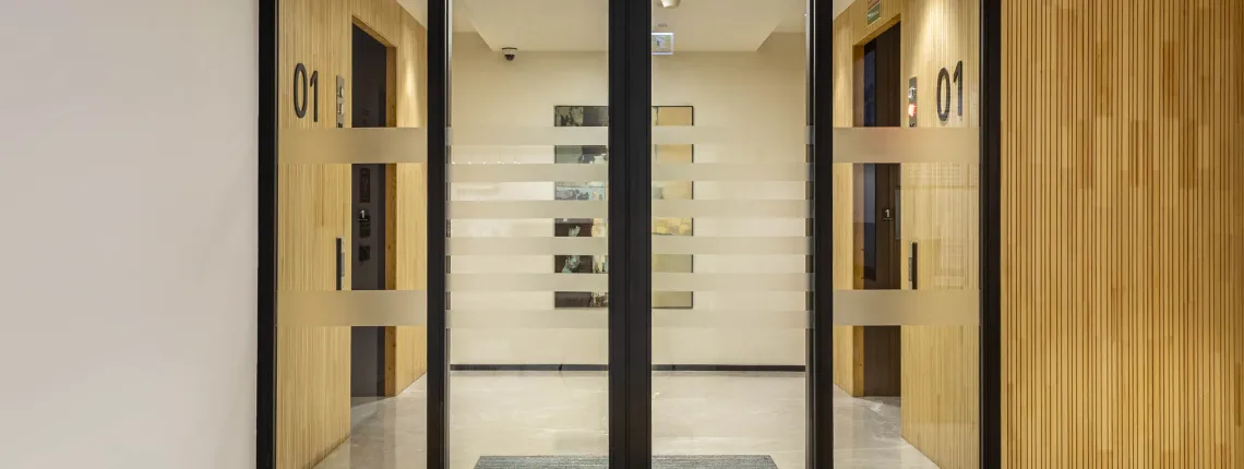 Automatic fire-rated sliding glass doors with black frames leading to a hallway with numbered doors.