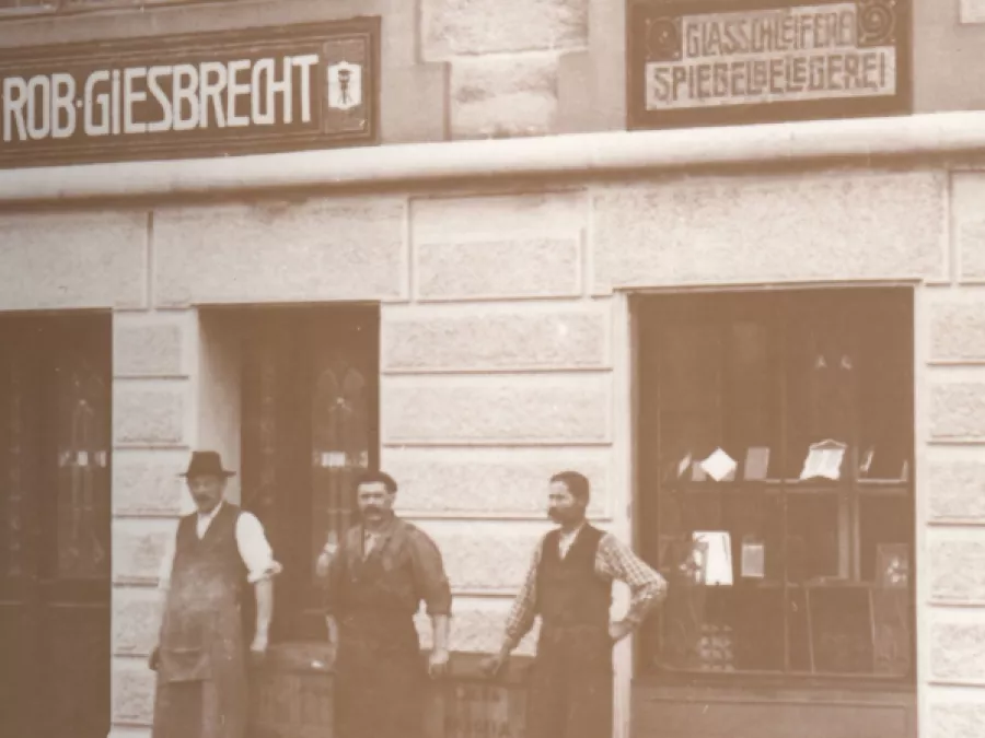 Giesbrecht History 1884 - Junkergasse, Bern Historical Vetrotech image showing a storefront with period signage and men, highlighting its long history.